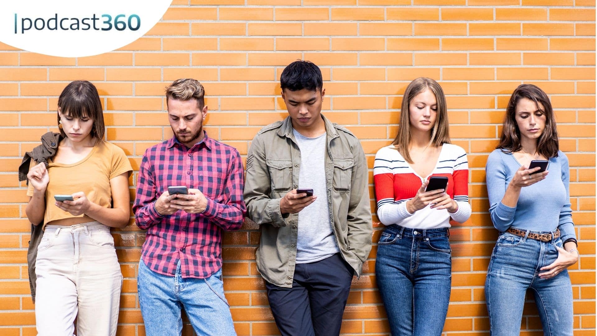 Fünf junge Erwachsene stehen vor einer Backsteinmauer und schauen alle auf ihre Smartphones.