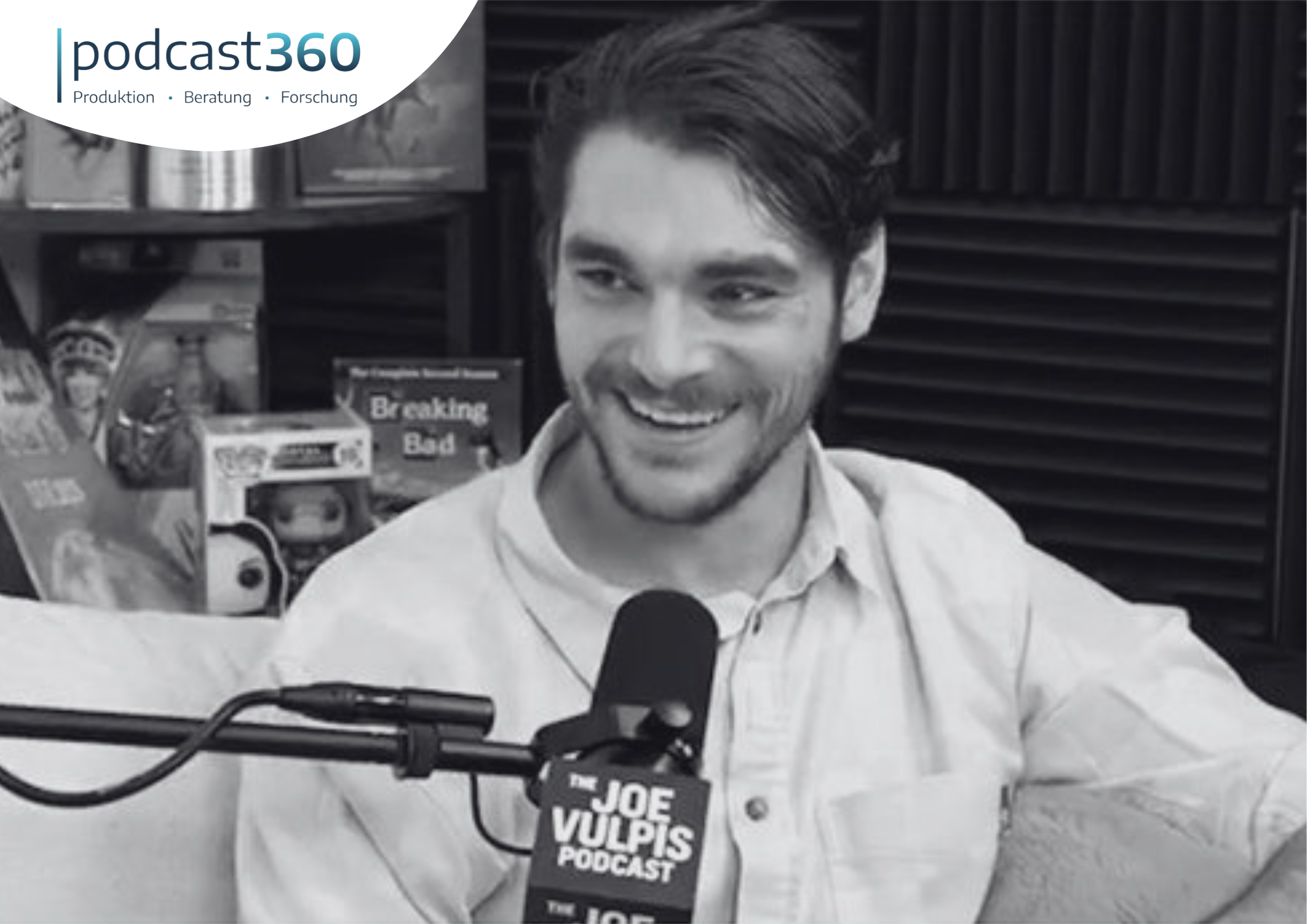 RJ Mitte lächelt während eines Interviews in das Mikrofon des Podcasts von Joe Vulpis.